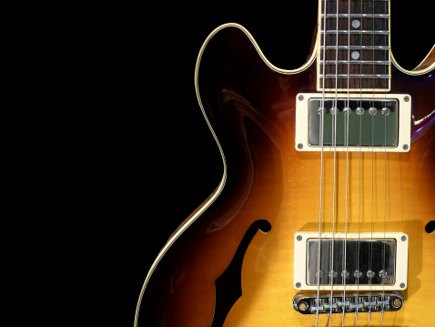 Close-up of vintage semi acoustic electric jazz guitar on black background.