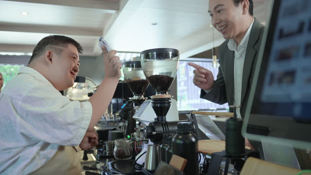 Young Asian man with disabilities receiving an order from handsome customer man wearing business suit in the morning for making special hot coffee at coffee shop.  Cafe hiring people with disabilities in order to have equal opportunity.
