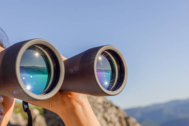 Close up Young woman holding binoculars looking mountains background.