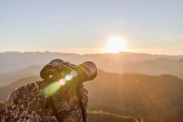 binoculars on top of rock mountain at beautiful sunset background.