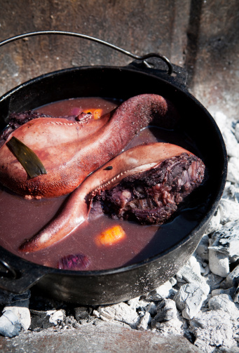 Two beef tongues being cooked in a cast iron pot on an open fire.