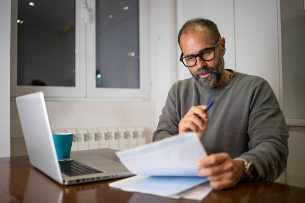 istock Mid adult man using calculator while going through bills and home finances 1566095615