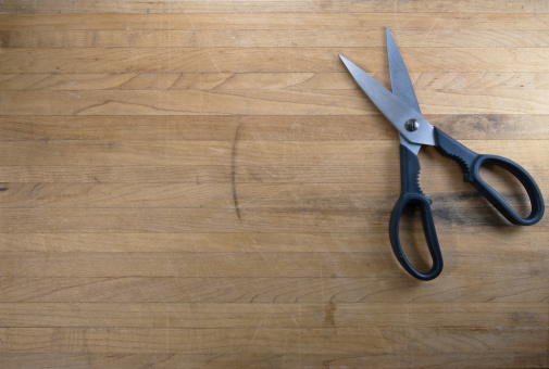 A pair of scissors sits half open on a worn butcher block counter top