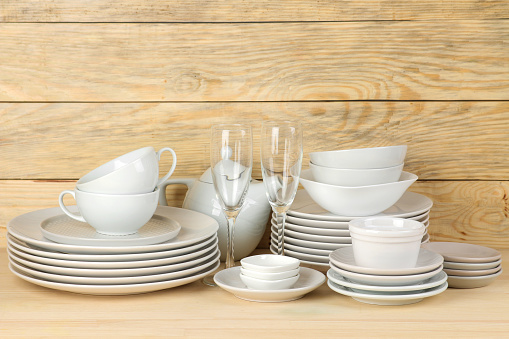 Piles of white ceramic tableware, plates, saucers and cups on a natural wooden background. kitchenware.