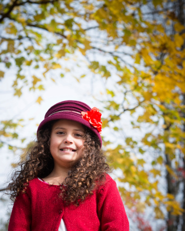 Cute young Hispanic girl with long curly hair plays in the park on an Autumn day.
