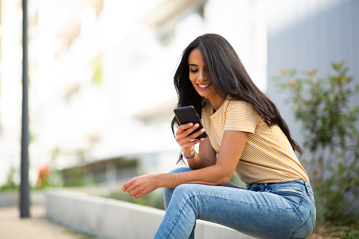 Portrait of smiling young woman sitting outside using mobile phone