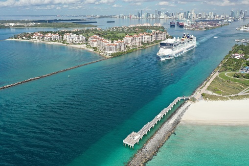 Miami Beach, Florida - May 23, 2020 - Aerial view of cruise ship leaving Port Miami on sunny tranquil summer morning with Fisher Island, Port Miami and city skyline in background.
