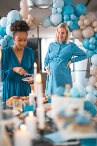 Dressed in a blue tunic, a beautiful mom-to-be smiles as she celebrates the arrival of her baby boy with her closest female friends. Balloons and decorations in shades of blue fill the room.