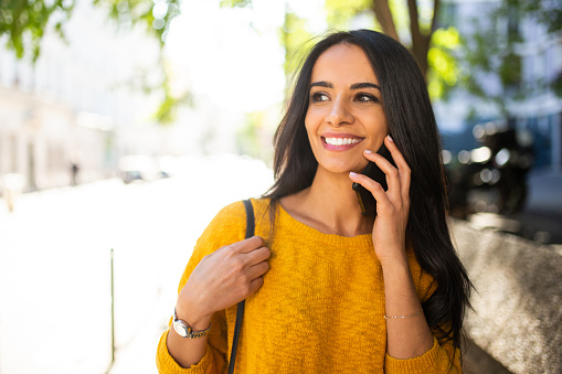 Close up portrait of smiling young woman walking and talking on cellphone in city