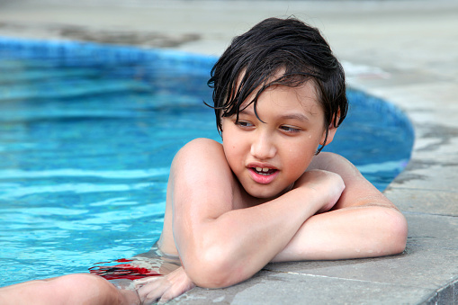 A young teenage Eurasian boy of Indonesian and British descent at the side of a swimming pool in Bali, Indonesia.