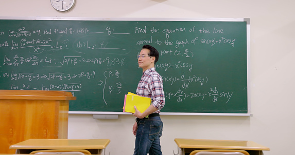 asian senior male calculus confident professor is walking in college classroom with textbooks