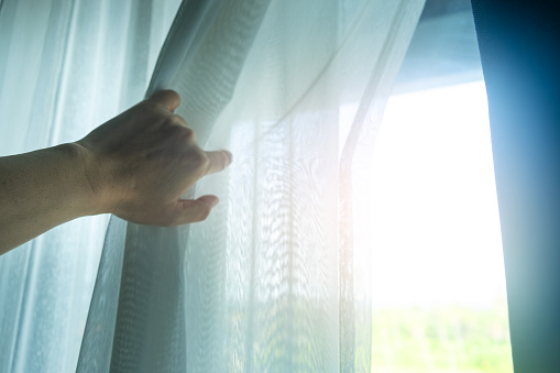 A woman's hand opens the curtains on the window and looks out at the beautiful view in the morning.