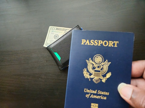 Wallet with Cash In The Background and A Hand Holding A USA Passport