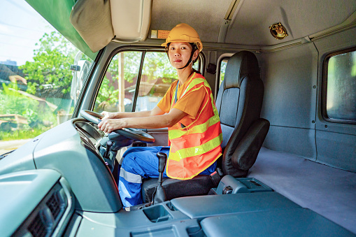 Portrait woman truck driver sitting in driver seat of a trailer truck, looking at camera