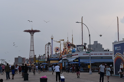 Brooklyn, New York City, USA - May 22, 2022 - Locals and tourists take an evening stroll on the Riegelmann Boardwalk while others go on Rides in the Luna Park in Coney Island.