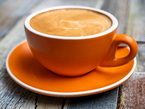 Mug with a saucer with cappuccino coffee on a diary with a handle with glasses on a wooden table in a coffee house