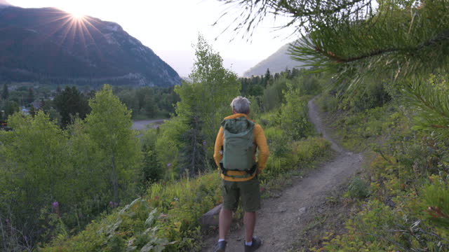 Senior man hikes along mountain trail at sunrise, takes pic