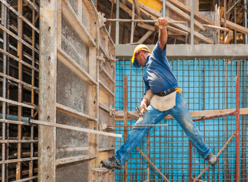Authentic construction worker in a difficult balancing position between scaffold and formwork frame