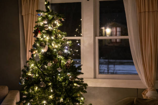 Beautiful Christmas ornaments hanging on the tree - window curtains open and snow falling outside. Shot at Nighttime - holidays concepts