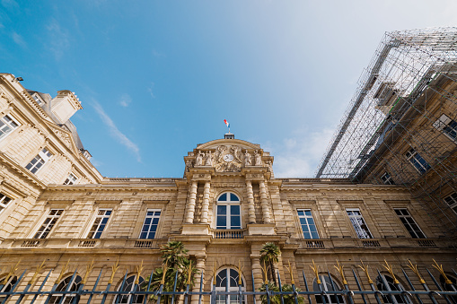 Paris, France - May 21, 2023: Low angle view of the Luxembourg Palace in 2023. The Jardin du Luxembourg (known in English as the Luxembourg Garden, or Senate Garden) is located in the 6th arrondissement of Paris, France. Creation of the garden began in 1612 when Marie de' Medici, the widow of King Henry IV, constructed the Luxembourg Palace as her new residence. The garden today is owned by the French Senate, which meets in the Palace. It covers 23 hectares and is known for its lawns, tree-lined promenades, tennis courts, flowerbeds, as well as picturesque Medici Fountain, built in 1620.