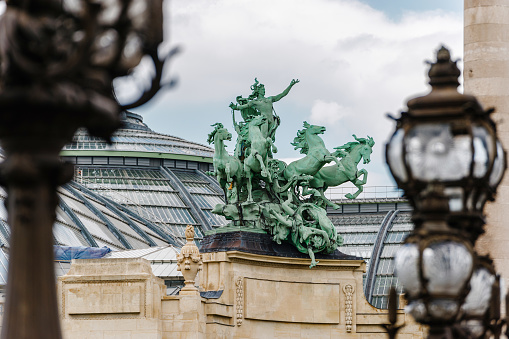 Paris, France - May 20, 2023: Bronze statue representing Harmony triumphing over Discord on the roof of the Grand Palais. 
The Grand Palais des Champs-Élysées (English: Great Palace of the Elysian Fields), commonly known as the Grand Palais, is a historic site, exhibition hall and museum complex located at the Champs-Élysées in the 8th arrondissement of Paris, France. Construction of the Grand Palais began in 1897 to prepare for the Universal Exposition of 1900. The bronze statue showing the group Harmony triumphing over Discord on the roof of the Grand Palais is by the sculptor Georges Récipon.