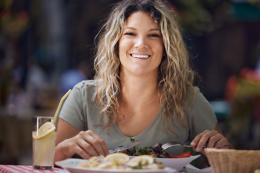 Happy woman enjoying while having a meal during spring day in a restaurant and looking at camera.