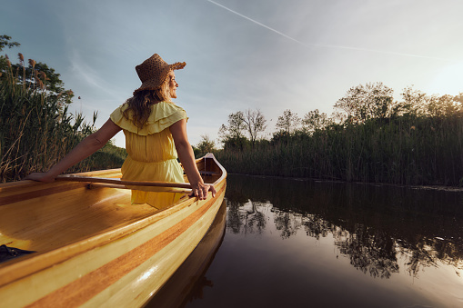 Back view of young happy woman spending a spring day in a boat at river. Copy space.