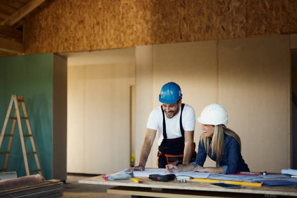 istock Happy female inspector and manual worker reading housing plans at construction site. 1566600382