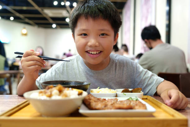 A cheerful little Asian boy enjoying a freshly served traditional Taiwanese-style meal, particularly a braised pork rice set, in a restaurant