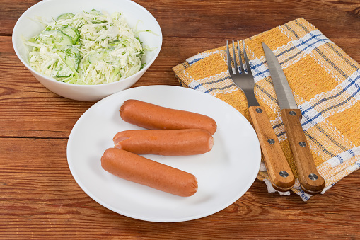 Serving of the steamed thin Vienna sausages with green vegetable salad on the rustic table