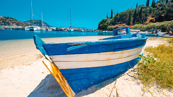 Old blue boat moored at sandy beach by harbor against clear sky during sunny day