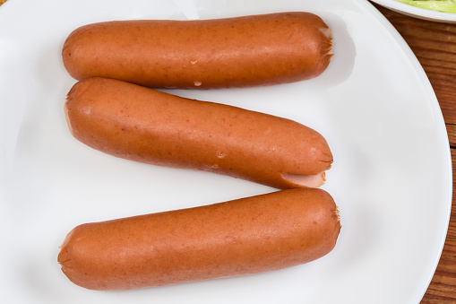 Steamed thin parboiled sausages, known as Vienna sausages, or frankfurters on a white dish, top view