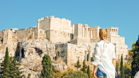Rear view of female tourist admiring ancient Acropolis of Athens while standing on Areopagus rock against clear blue sky during summer vacation at Greece