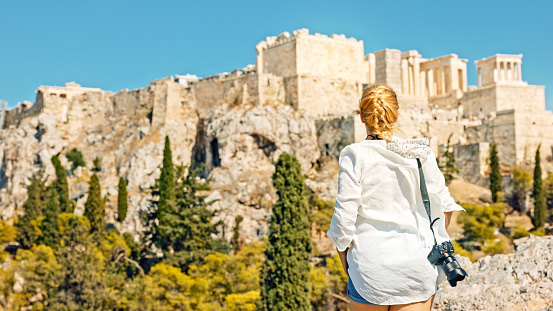 Rear view of female tourist admiring ancient Acropolis of Athens while standing on Areopagus rock against clear blue sky during summer vacation at Greece