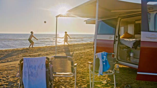pareja jugando voleibol en la playa fuera de la autocaravana - outdoor chair beach chair sarong fotografías e imágenes de stock