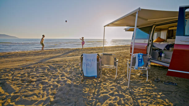 pareja jugando voleibol en la playa fuera de la autocaravana - outdoor chair beach chair sarong fotografías e imágenes de stock