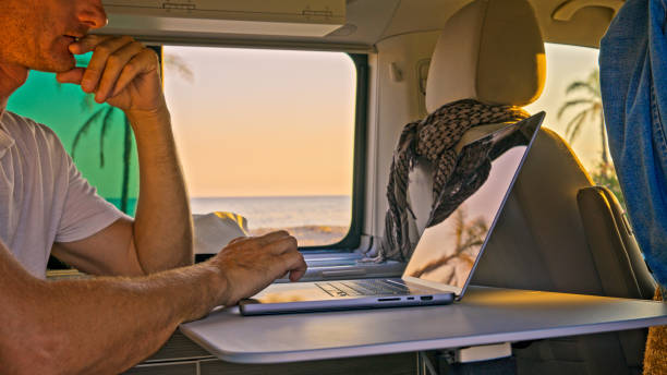 istock Man using laptop in motor home against beautiful sea during sunset 1566665540