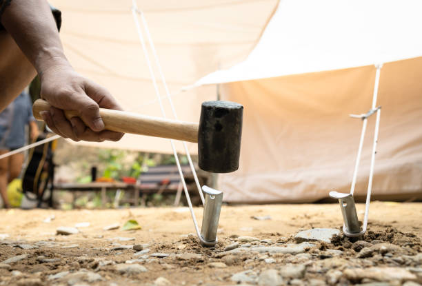 mão do homem segurando um martelo de borracha, martelando o aço de alumínio estaca estacas prego, tenda de fixação para acampar, bater ou bater âncora da barraca no chão, martelo com cabeça de borracha, cabo de madeira - rubber mallet - fotografias e filmes do acervo