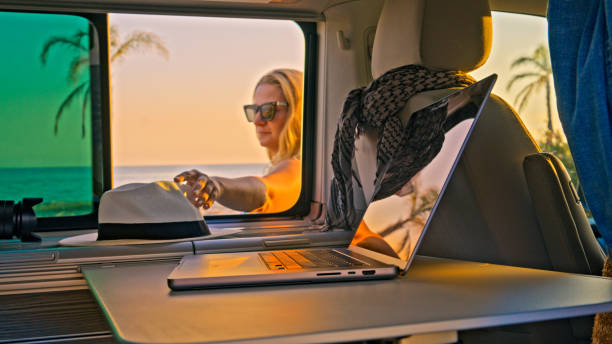 istock Woman picking up hat from camper van window at the beach 1566673038