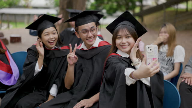 Asian Chinese students in graduation gown taking selfie with smartphone on graduation day