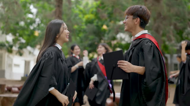 Asian male and female student in graduation gown chit chatting after graduation ceremony