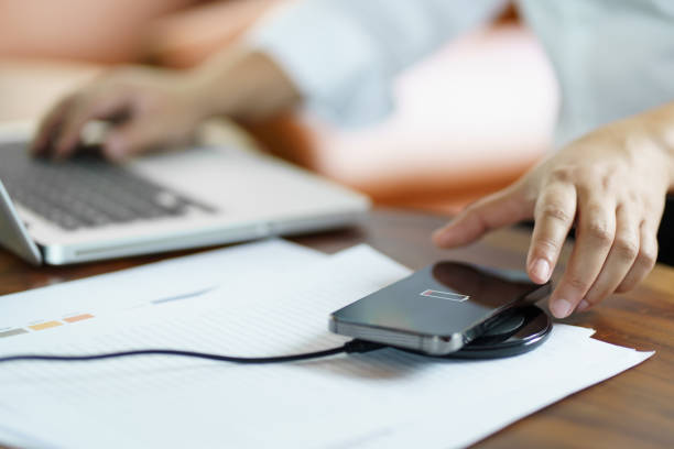 istock Charging mobile phone battery with wireless charging device in the table. Smartphone charging on a charging pad. Mobile phone near wireless charger Modern lifestyle technology concept 1566707017