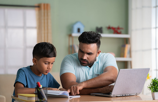 Indian father helping his son for reading while working on laptop at home - concept of Educational assistance, Parental guidance and Multitasking.