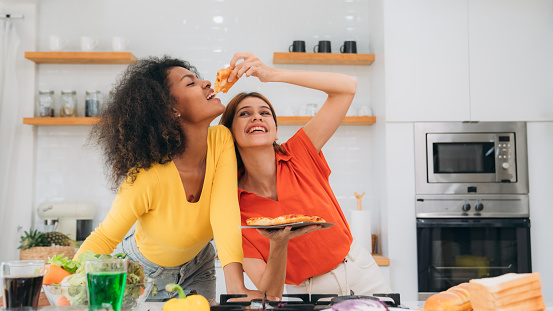 Happy Young Woman Cooking Together in the Kitchen. Cheerful Friends Enjoying a Delicious Pizza Meal Together.Young LGBT Couple Enjoying Delicious Meal. Cooking and Eating Together.