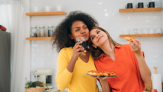 Happy Young Woman Cooking Together in the Kitchen. Cheerful Friends Enjoying a Delicious Pizza Meal Together.Young LGBT Couple Enjoying Delicious Meal. Cooking and Eating Together.