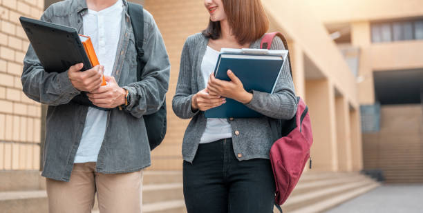 istock Two students holding book and laptop talking together discussing about exam preparation, study for test preparation in University. 1566750429