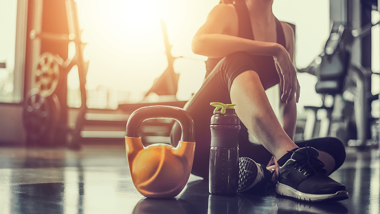 Concepts healthy lifestyle and workout. Bodybuilder, Workout, Fitness, Gym. Young asian woman sitting taking a break relaxing after exercise with a whey protein and dumbbell placed beside at gym.