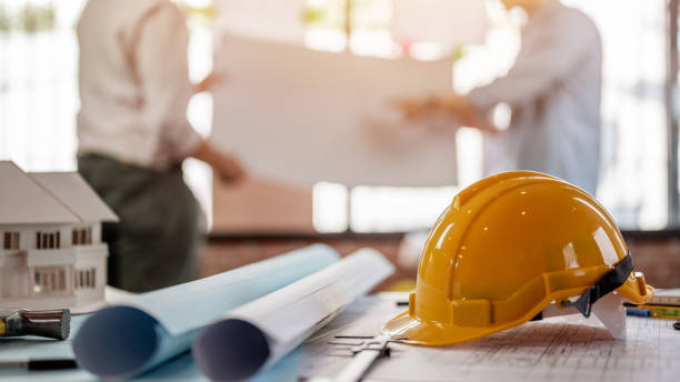 istock Safety helmets and blueprint on the table at site construction. Architect, Engineer and businessman read planning background. 1566754236