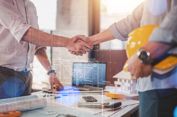 istock engineers and team shake hands around blueprint and structure with dashboard smart home hud. 1566757499