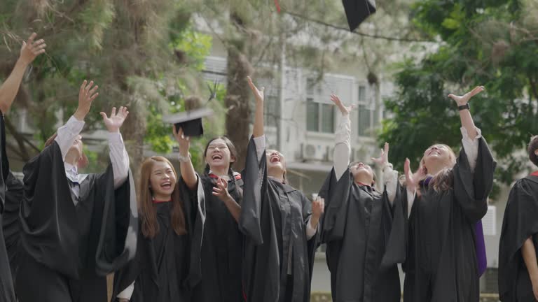 Asian college students tossing mortarboard up in the air after graduation ceremony